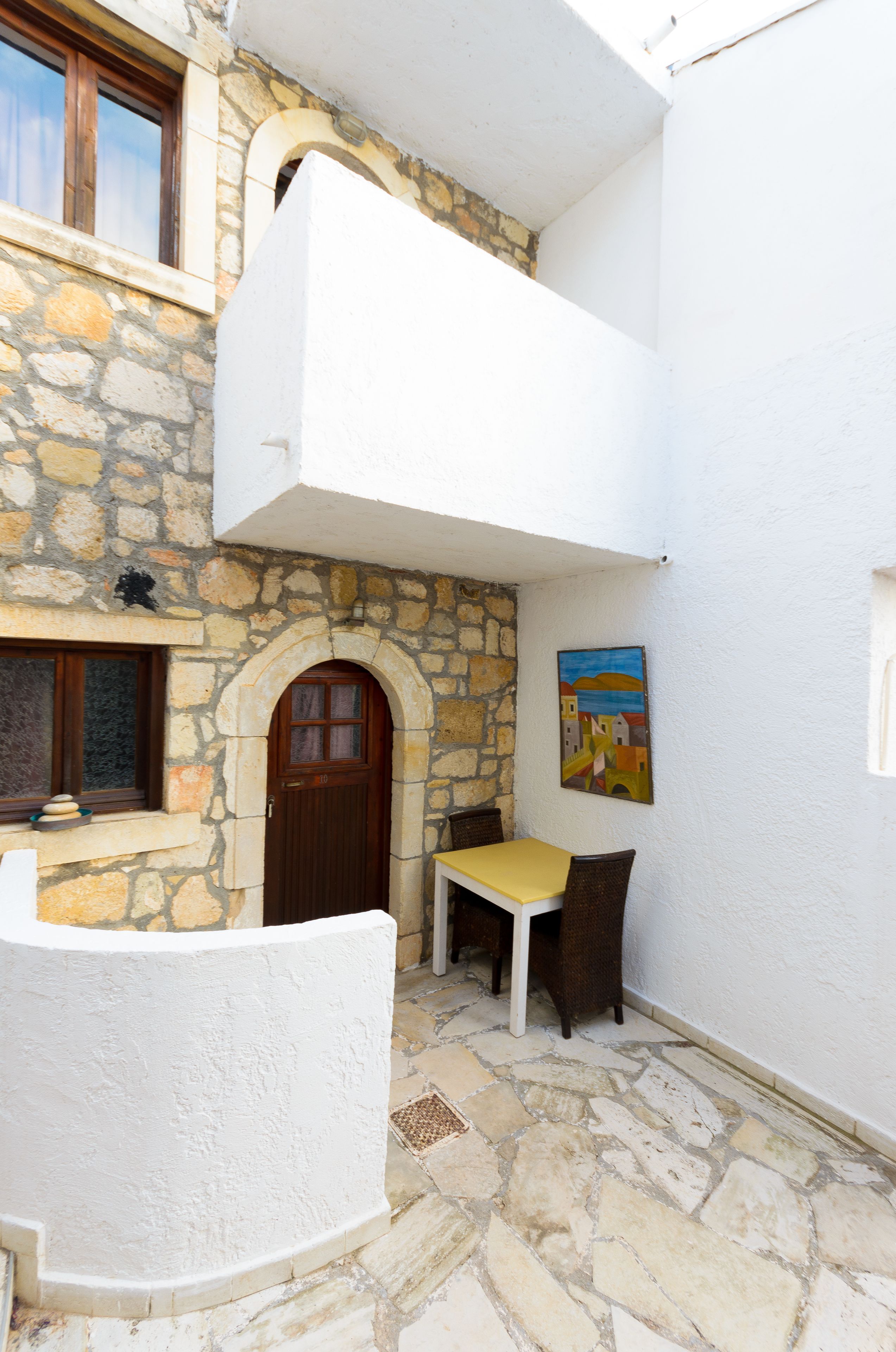 A stone building with a white exterior, a wooden door, a small table with chairs, and a painting on the wall.