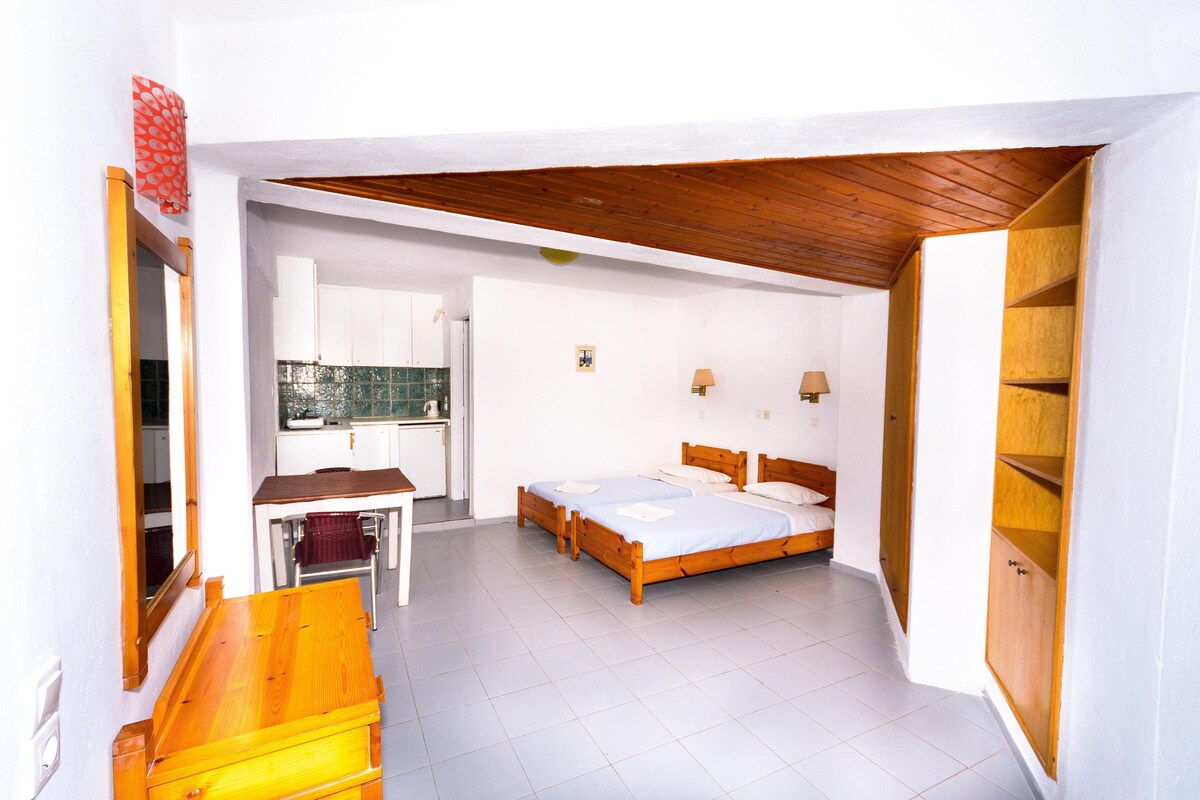 A bedroom with two beds, a wooden desk, and a kitchenette.
