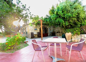 A stone building with a patio area featuring a table and chairs, surrounded by lush greenery and a stone wall. - Classic Apartments (Hersonissos)