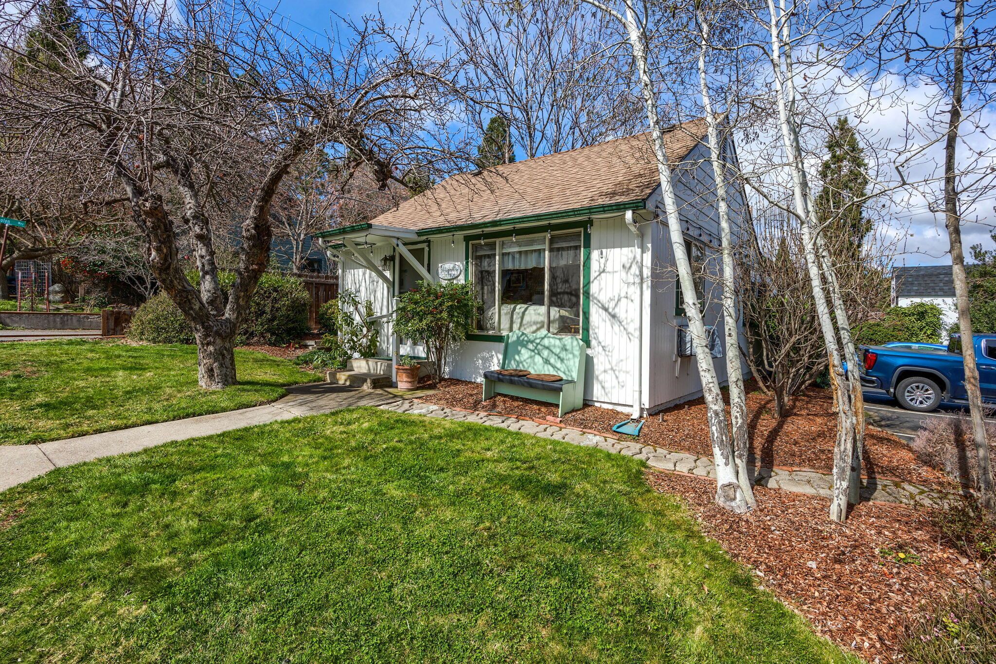 A small, single-story house with a front porch, a pathway leading to the entrance, and a blue car parked nearby.