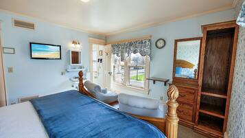 A bedroom with a bed, two chairs, a dresser, a mirror, a clock, and a window with a view of the outdoors.