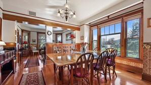 Un comedor amplio con una mesa y sillas de madera, ventanas grandes que ofrecen vistas al exterior y un candelabro.