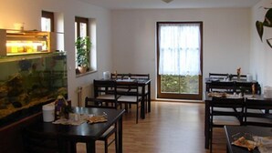 Un espace repas avec des tables et des chaises en bois, un aquarium et une grande fenêtre agrémentée de rideaux.