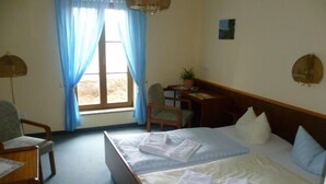 Une chambre d’hôtel avec deux lits, un bureau, une chaise, une plante en pot et une fenêtre avec des rideaux.