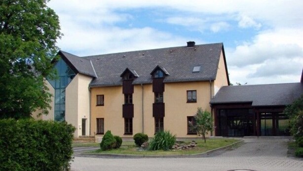Un grand bâtiment à deux étages, doté d’une façade symétrique, avec une entrée centrale flanquée de deux fenêtres et un petit espace porche.