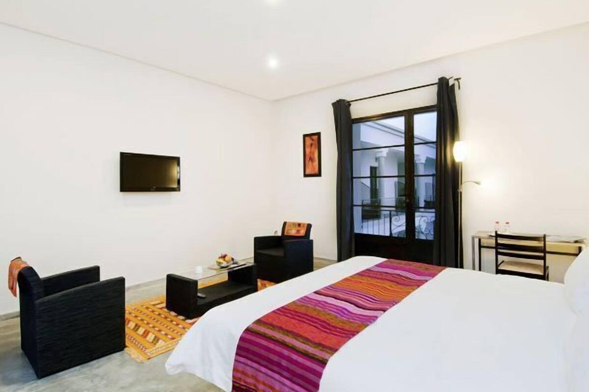 Habitación de hotel con cama, escritorio, silla, televisor y ventana con cortinas.