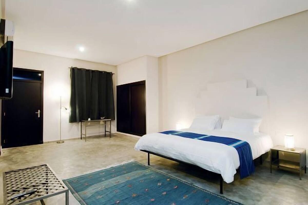 Un dormitorio con cama, televisión, escritorio y ventana con cortinas.