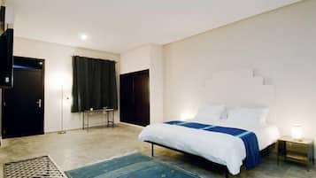 Un dormitorio con cama, televisión, escritorio y ventana con cortinas.