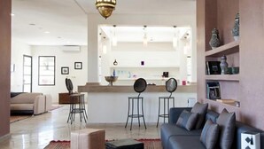 A modern living room with a sofa, a coffee table, and a dining area with stools. - Villa Agapanthe (Fes)