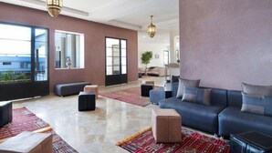 A spacious living room with a large sofa set, a coffee table, and a rug. There are two large windows providing natural light and a view of the outdoors. - Villa Agapanthe (Fes)