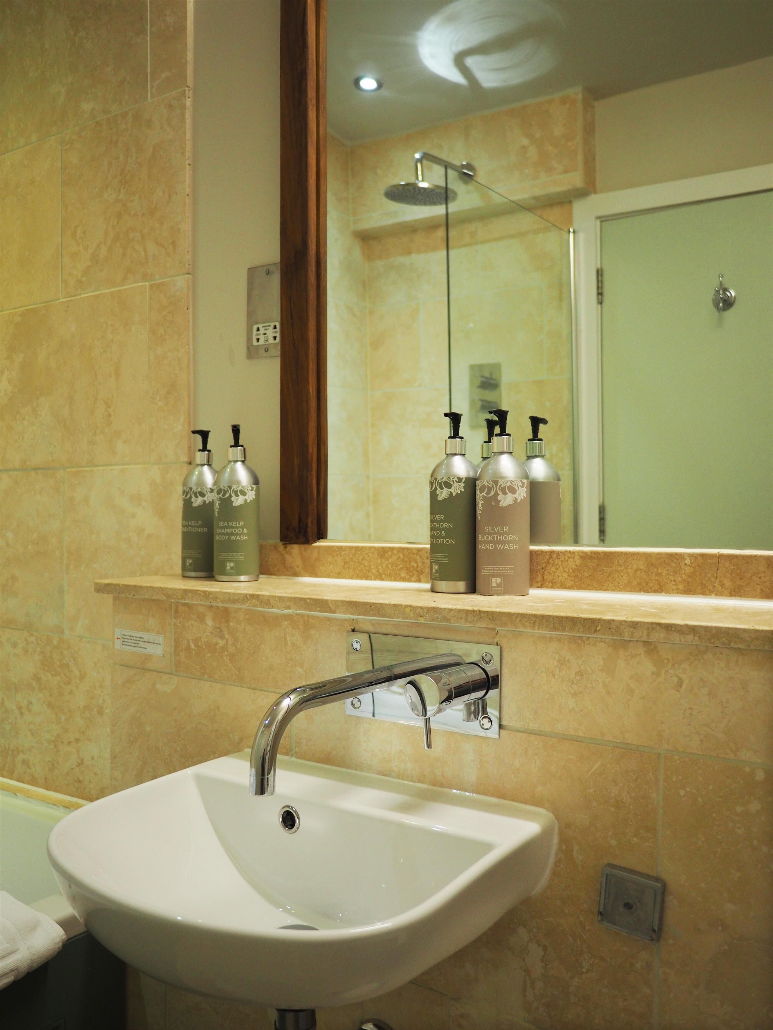 A bathroom with a white sink, a mirror, and a shower. There are bottles of shampoo and body wash on the counter.