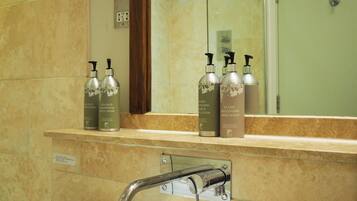 A bathroom with a white sink, a mirror, and a shower. There are bottles of shampoo and body wash on the counter.
