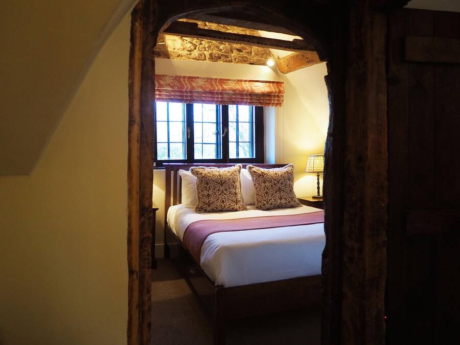 A bedroom with a wooden bed, patterned pillows, a window with curtains, and a lamp on a bedside table.