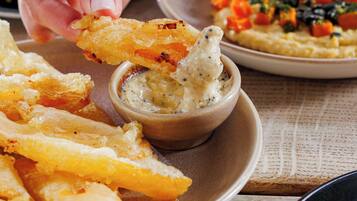 A hand dipping a fried item into a bowl of sauce.