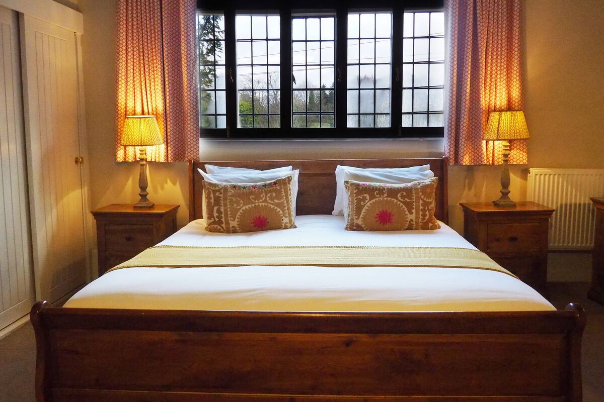 A neatly made bed with patterned pillows, two bedside lamps, and a window with curtains.
