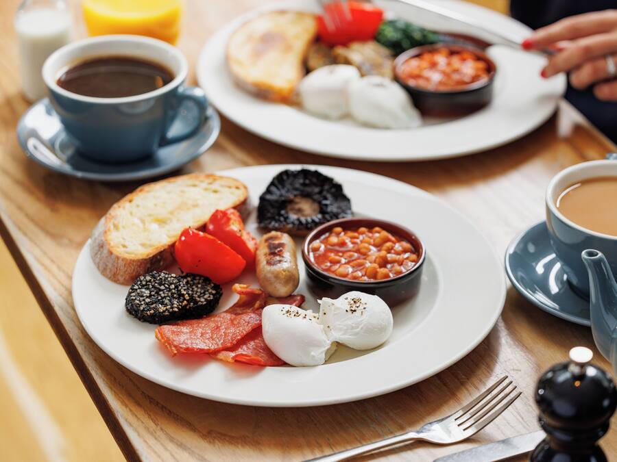 A breakfast setting with plates of eggs, bacon, tomatoes, beans, and toast.