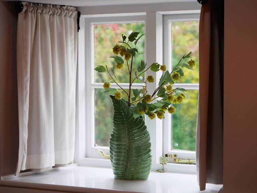 A window with a green leaf-shaped vase containing yellow flowers.