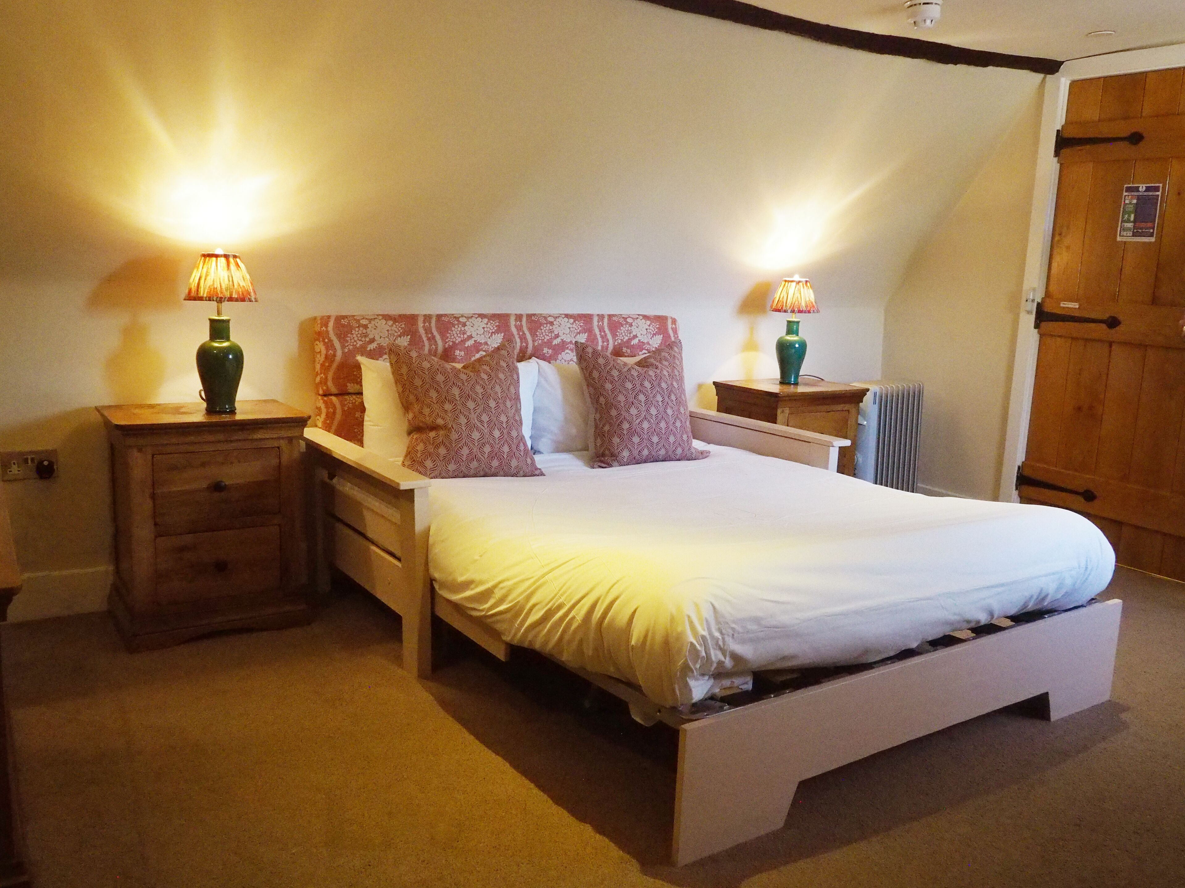 A bedroom with a bed, two bedside tables, lamps, a radiator, and a wooden wardrobe.