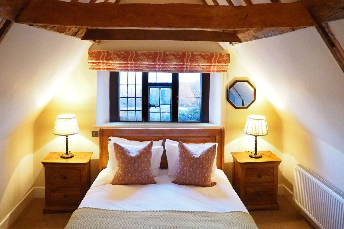 A bedroom with a large bed, two bedside tables with lamps, a window with a view, and a mirror on the wall.
