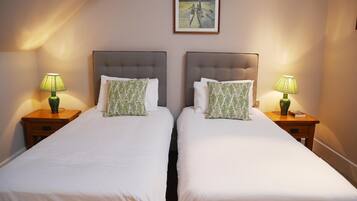 A hotel room with two beds, each with a green leaf-patterned pillow and a green lamp on a wooden nightstand.
