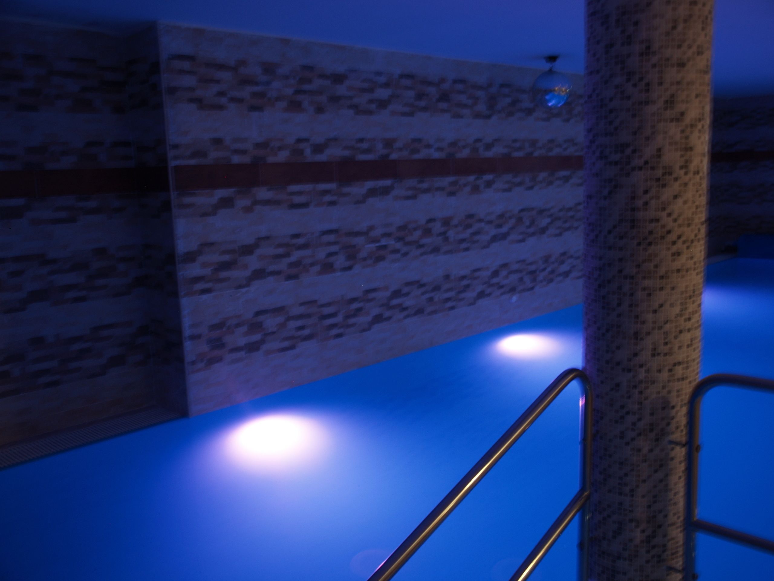 A bathroom with a blue-lit floor, a metal handrail, and tiled walls.