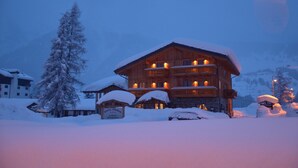 Een meerhoog gebouw van hout met balkons, omringd door met sneeuw bedekte bomen en een bord waarop een restaurant wordt aangegeven.