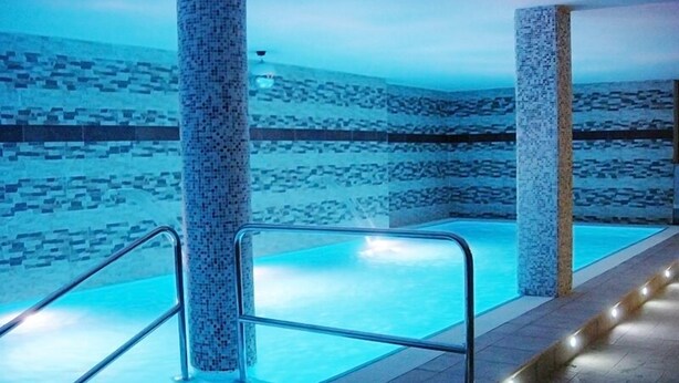 Een binnenzwembad met helderblauw water, betegelde wanden en een betegelde vloer.