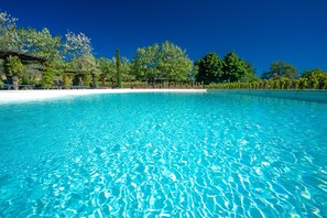 A clear blue pool surrounded by trees and a white sandy beach. - Relais Campiglioni (Montevarchi)