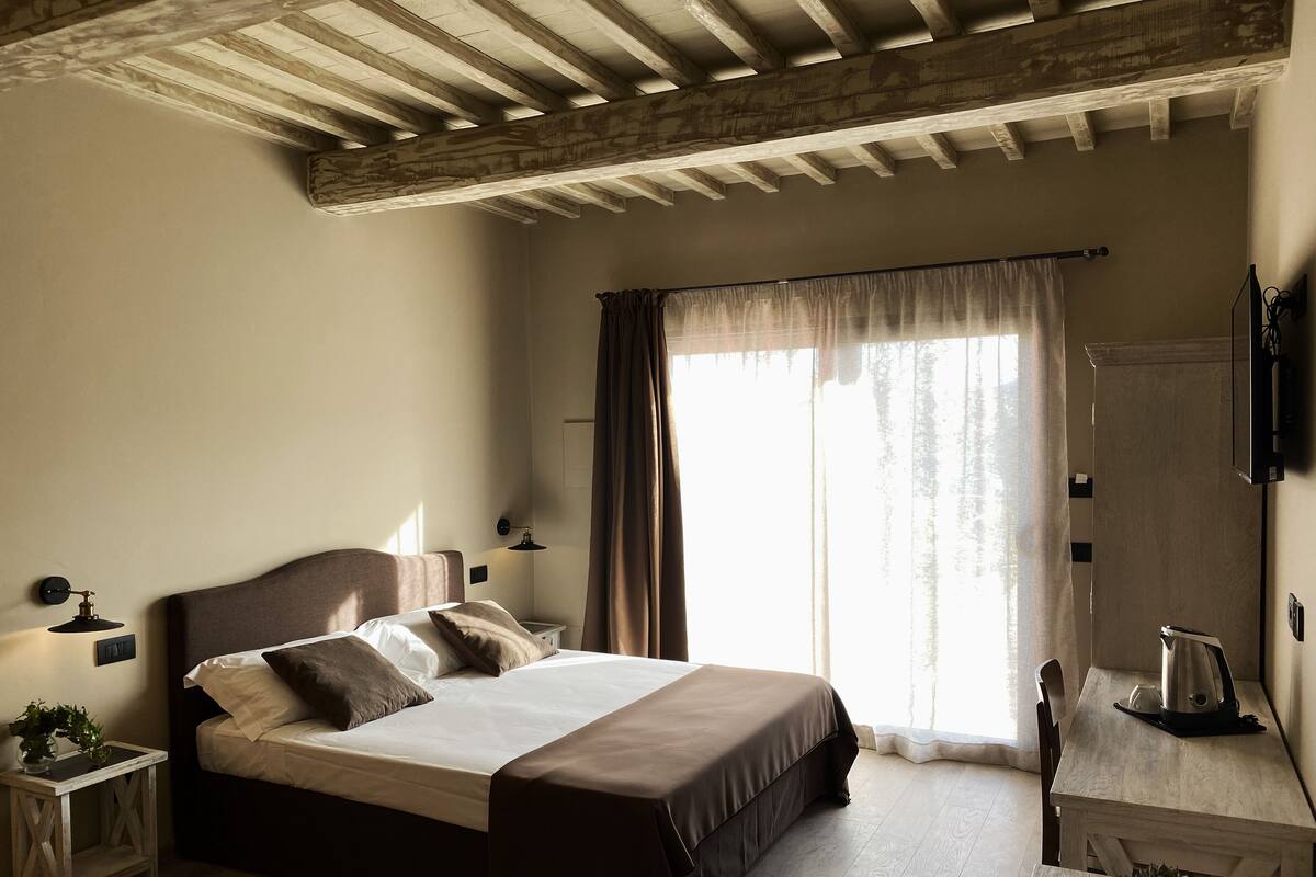 A bedroom with a large bed, bedside tables with lamps, a wooden desk, and a window with curtains.