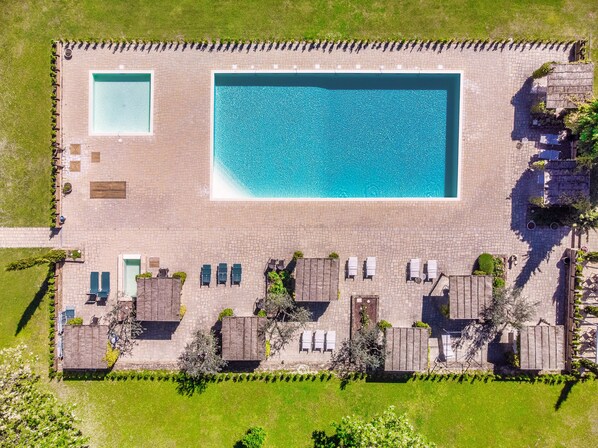 An aerial view of a hotel with a large rectangular pool, multiple lounge areas with umbrellas, and a well-maintained lawn. - Relais Campiglioni (Montevarchi)