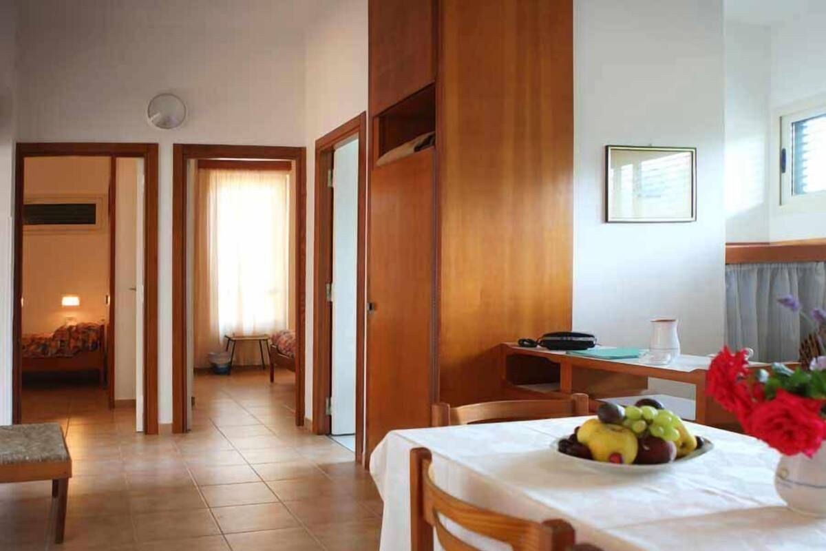 A hotel room with a dining area featuring a table set with fruit and a vase of flowers.