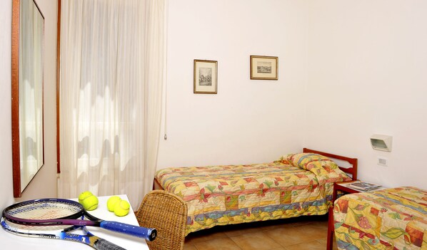 Un dormitorio con dos camas, una ventana con cortinas, un espejo y una mesa con raquetas y pelotas de tenis.