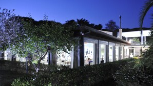 Un edificio moderno con grandes ventanales de vidrio, rodeado de vegetación.
