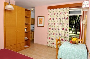Een kamer met een houten garderobe, een eettafel met een tafelkleed met bloemenprint, en een raam met bloemen gordijnen.