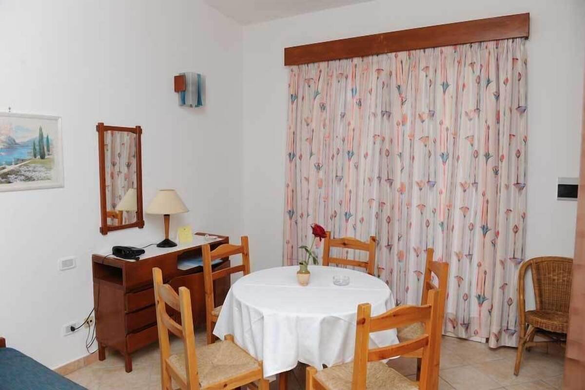 A dining area with a round table, wooden chairs, a lamp, and a floral curtain.
