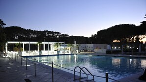 Una piscina con zona hundida, rodeada por una pérgola blanca y palmeras.