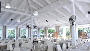 Un comedor amplio con mesas y sillas blancas, ventanas grandes y ventiladores de techo.