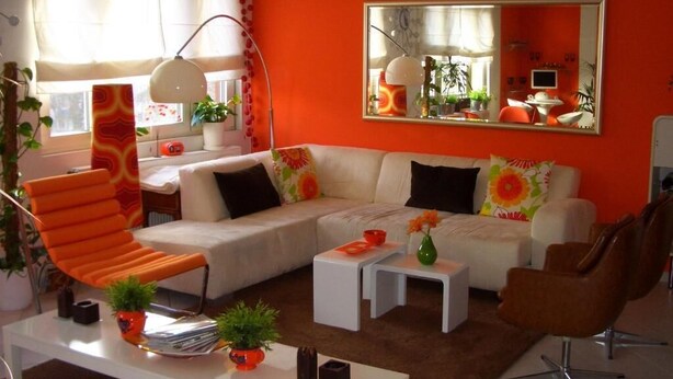 Un salon moderne avec un canapé blanc, un fauteuil orange et un grand miroir qui reflète la pièce.