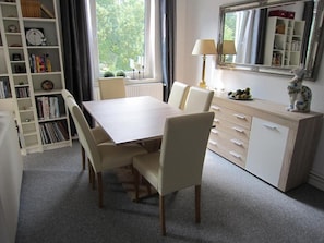 A dining area with a table and chairs, a bookshelf, a lamp, and a dresser.