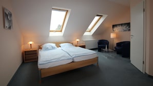 Une chambre à coucher comprenant un lit, deux tables de chevet, un bureau, deux chaises et un radiateur.