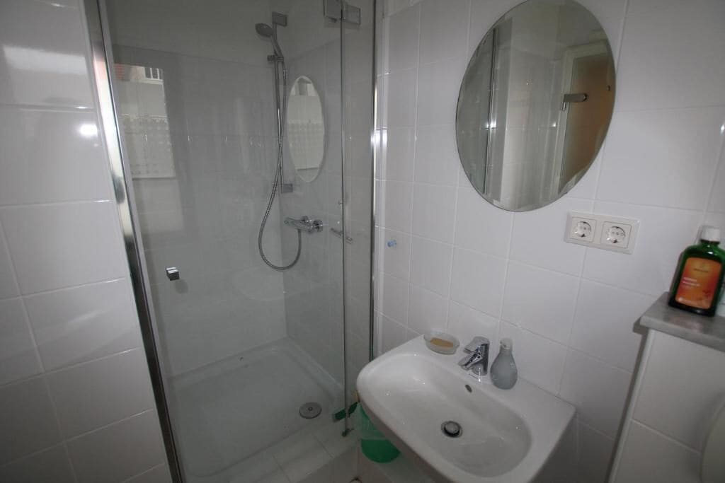A bathroom with a glass-enclosed shower, a sink with toiletries, and a mirror.