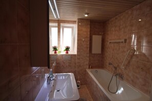 A modern bathroom with a large bathtub, a double sink, and a window with potted plants.