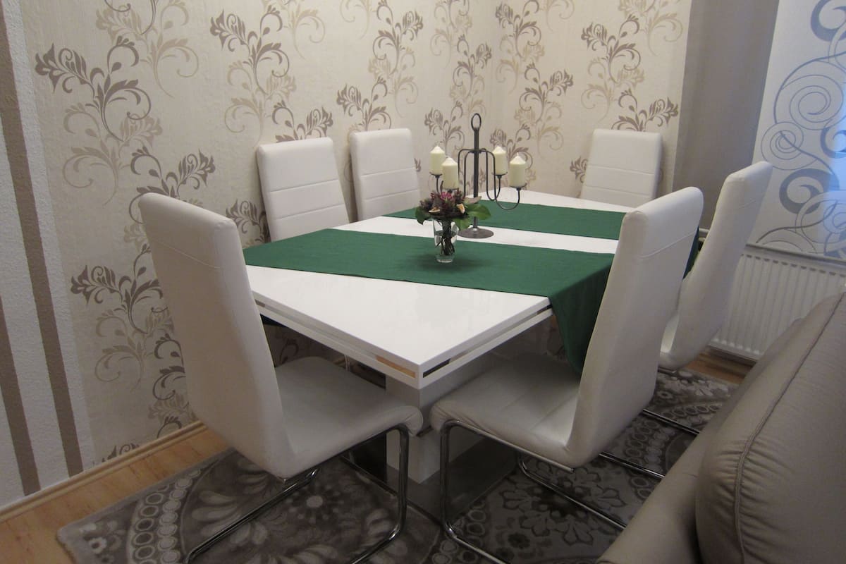 A dining area with a white table, green table runner, and six white chairs.
