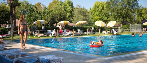 Zona de piscina con sillas de descanso, sombrillas y solárium.