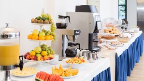 Un bufé con varias frutas, una máquina de café y un dispensador de zumos.