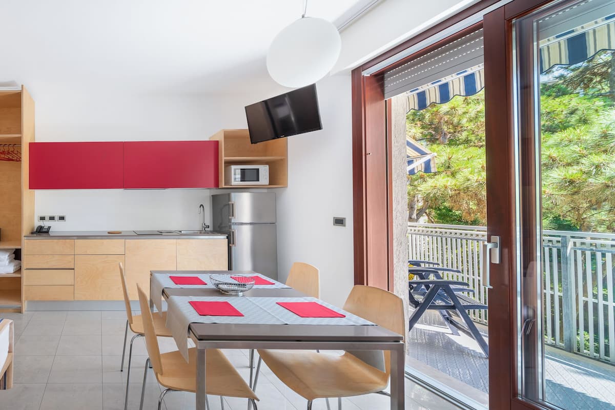 A compact hotel room with a bed, a small kitchenette, a dining area, and a balcony with a view.