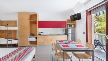 Una habitación de hotel compacta con cama, una kitchenette pequeña, zona de comedor y balcón con vistas.