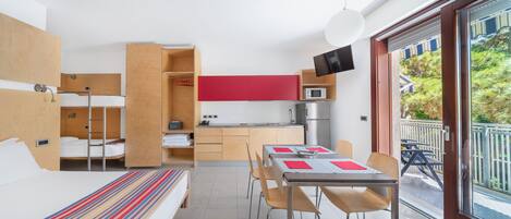 A compact hotel room with a bed, a small kitchenette, a dining area, and a balcony with a view.