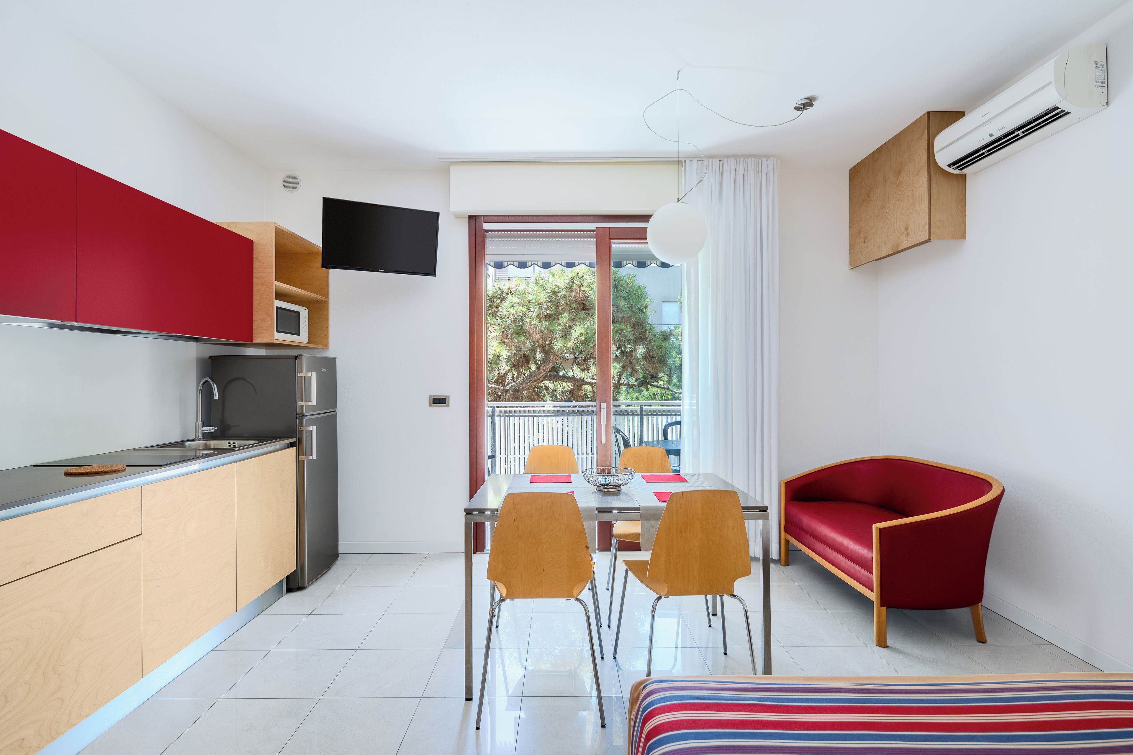 A compact kitchen with modern appliances, a dining area with a table and chairs, and a red sofa.