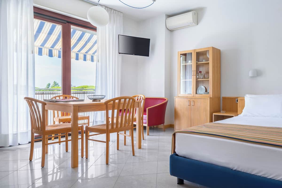 A hotel room with a bed, a desk with chairs, a television, a cabinet, and a window with curtains.
